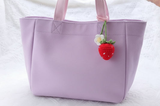 Crocheted strawberry pendant attached to a pink/ lilac handbag.